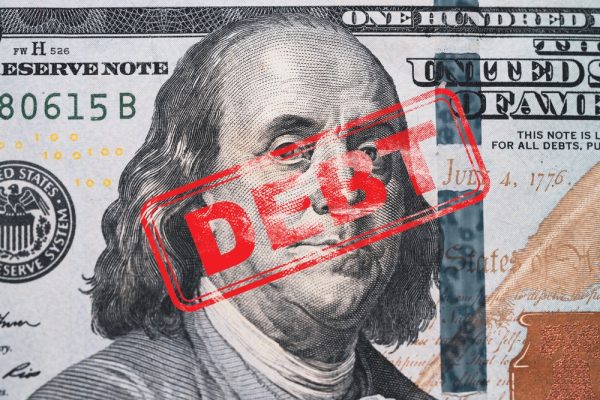 Top 5 Most Serious Consequences of Unpaid Tax Debt | Red stamp debt wording on Benjamin Franklin of one hundred American USD banknote for United States of America government debt ceiling concept.