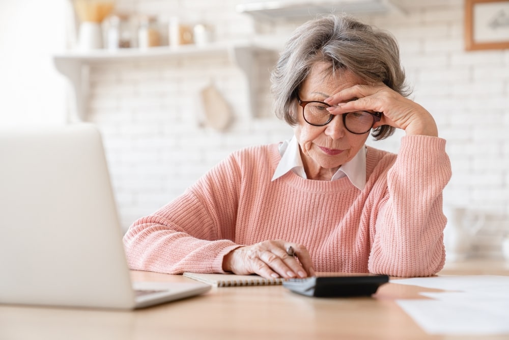 Senior woman calculating finances with laptop and calculator at home
