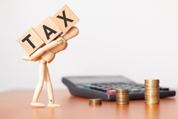 Wooden figure carrying tax blocks next to a calculator and stacked coins