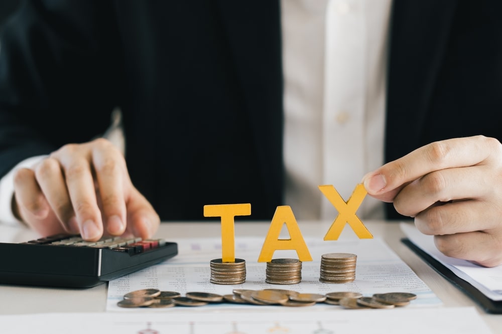 Businessperson stacking coins to spell TAX while calculating finances