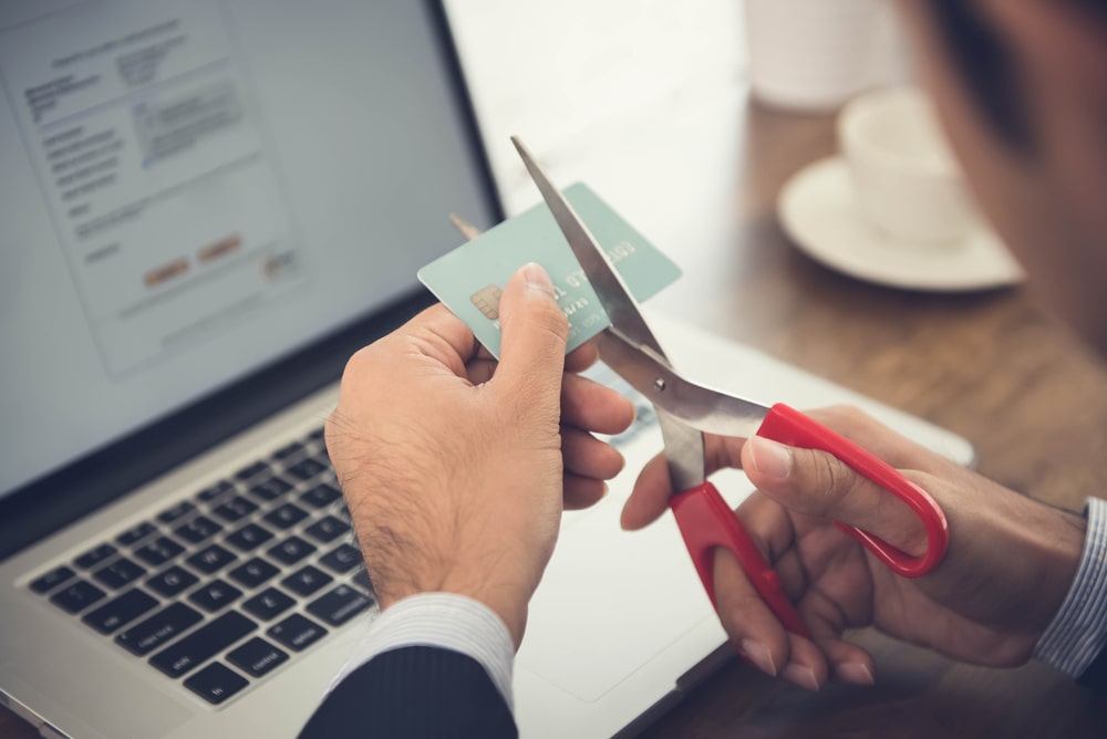 Person cutting up a credit card with scissors in front of a laptop