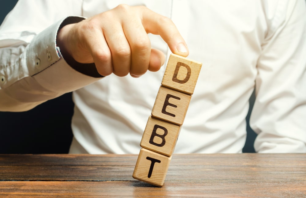Hand holding wooden blocks spelling the word DEBT on a table