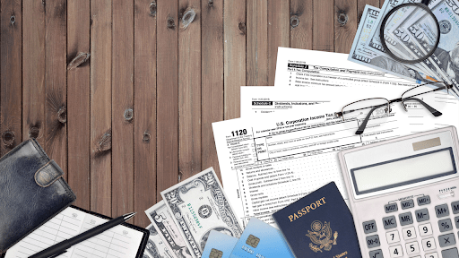 Tax forms, calculator, passport, cash, and financial documents on a wooden desk showing IRS debt passport restrictions