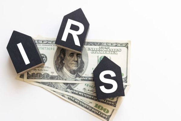 IRS debt payment options represented by wooden blocks spelling “IRS” on top of U.S. hundred-dollar bills.