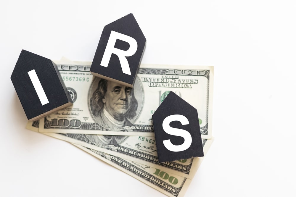 IRS debt payment options represented by wooden blocks spelling “IRS” on top of U.S. hundred-dollar bills.