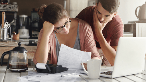 Couple reviewing tax documents and debt forgiveness paperwork on laptop at kitchen table