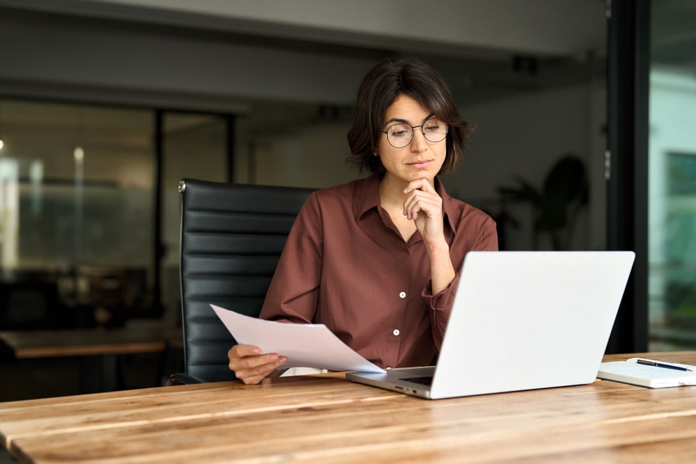 Woman reviewing documents and using a laptop, possibly checking her IRS debt offset status online.