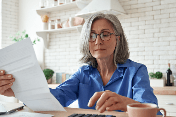 Senior woman with glasses reading IRS debt letter at kitchen table with concerned expression