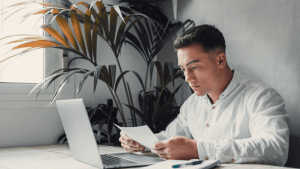 Professional man conducting IRS debt lookup review while examining tax documents at modern office desk with laptop and plants