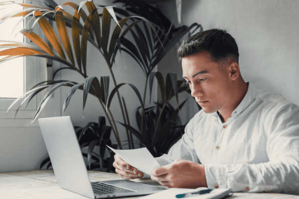 Professional man conducting IRS debt lookup review while examining tax documents at modern office desk with laptop and plants
