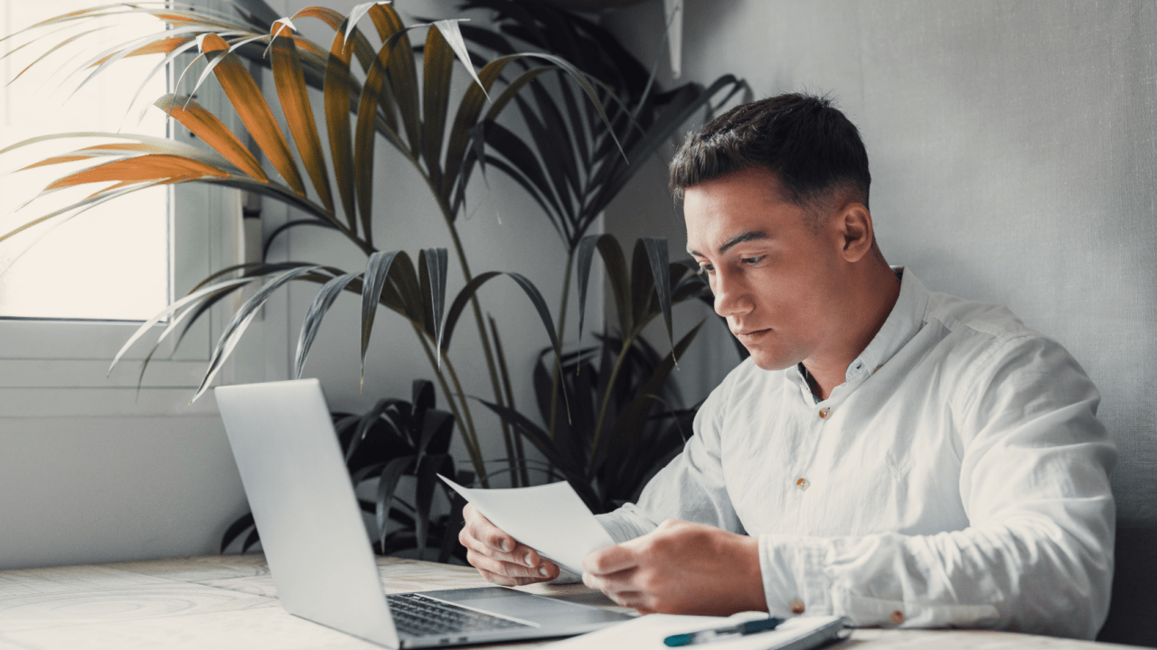 Professional man conducting IRS debt lookup review while examining tax documents at modern office desk with laptop and plants