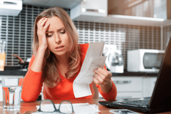 Overwhelmed woman holding head while reviewing bad debt tax write off documentation and researching tax deduction options on laptop