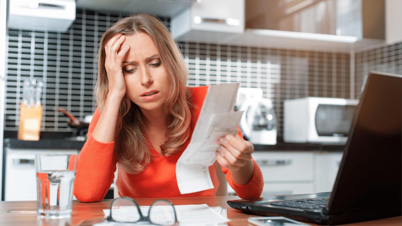 Overwhelmed woman holding head while reviewing bad debt tax write off documentation and researching tax deduction options on laptop