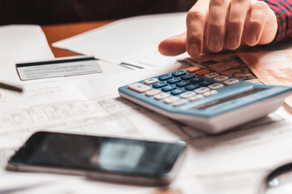Person calculating debt tax benefit deductions using calculator while reviewing tax documents and financial statements on desk