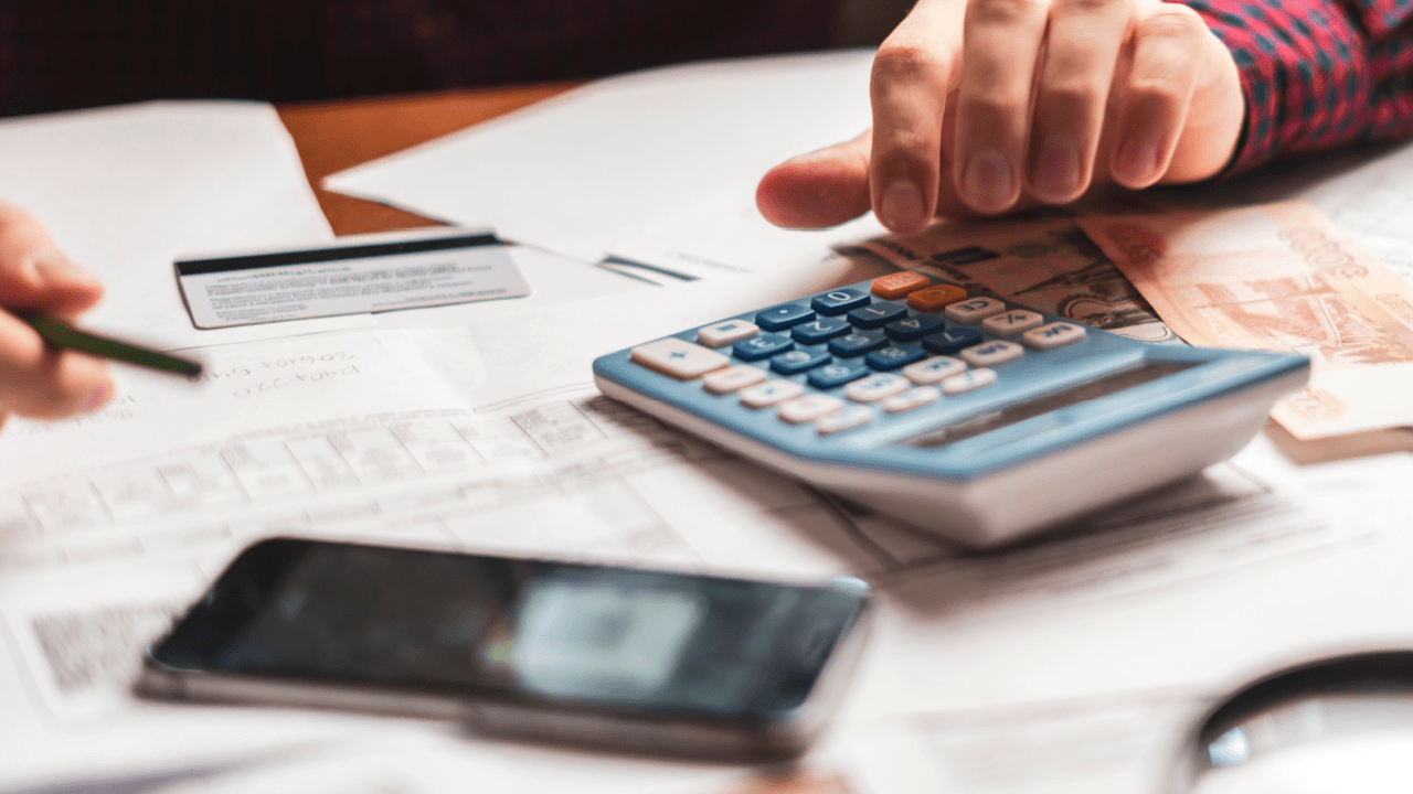 Person calculating debt tax benefit deductions using calculator while reviewing tax documents and financial statements on desk