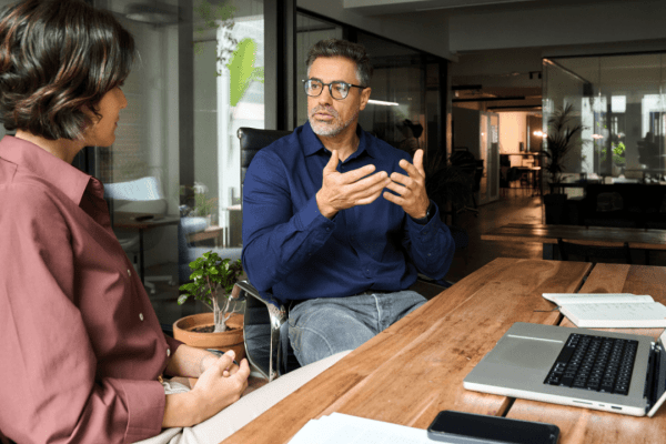 Financial advisor explaining IRS debt issuance costs to client during professional consultation in modern glass office with laptop and documents