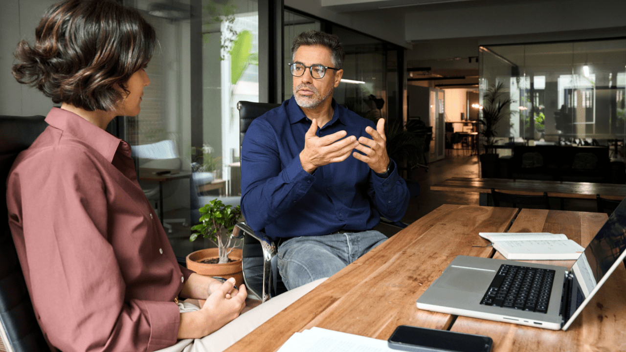 Financial advisor explaining IRS debt issuance costs to client during professional consultation in modern glass office with laptop and documents
