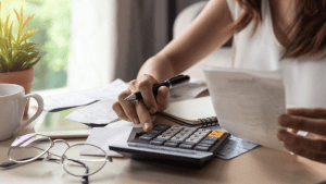 Woman calculating tax obligations while reviewing IRS debt lien list documents and financial paperwork at home office desk