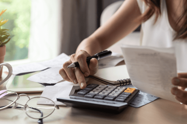 Woman calculating tax obligations while reviewing IRS debt lien list documents and financial paperwork at home office desk