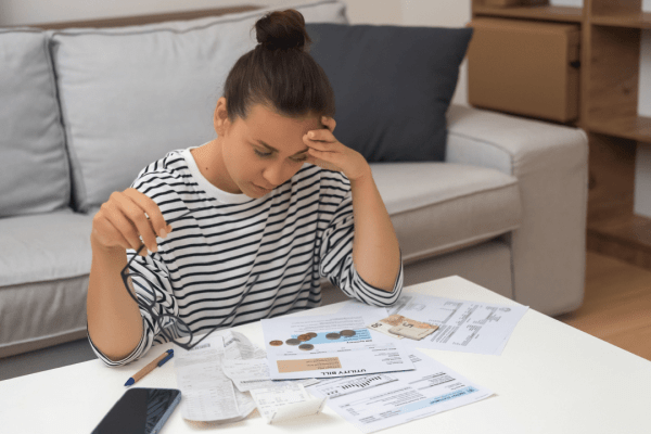 Overwhelmed woman holding glasses while reviewing bills and researching irs debt tax relief options at home coffee table