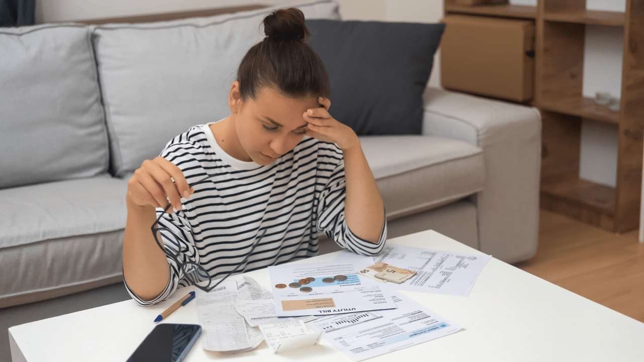 Overwhelmed woman holding glasses while reviewing bills and researching irs debt tax relief options at home coffee table