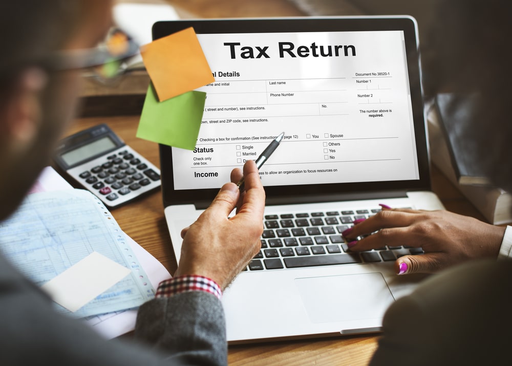 People reviewing a tax return form on a laptop with calculator and documents on the desk