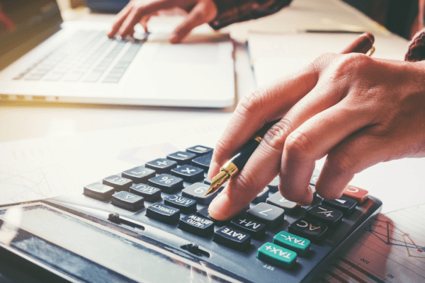 Person using calculator to determine how much money needed to settle my tax debt while reviewing financial documents and charts