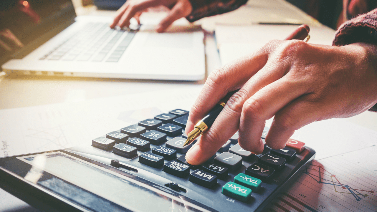 Person using calculator to determine how much money needed to settle my tax debt while reviewing financial documents and charts
