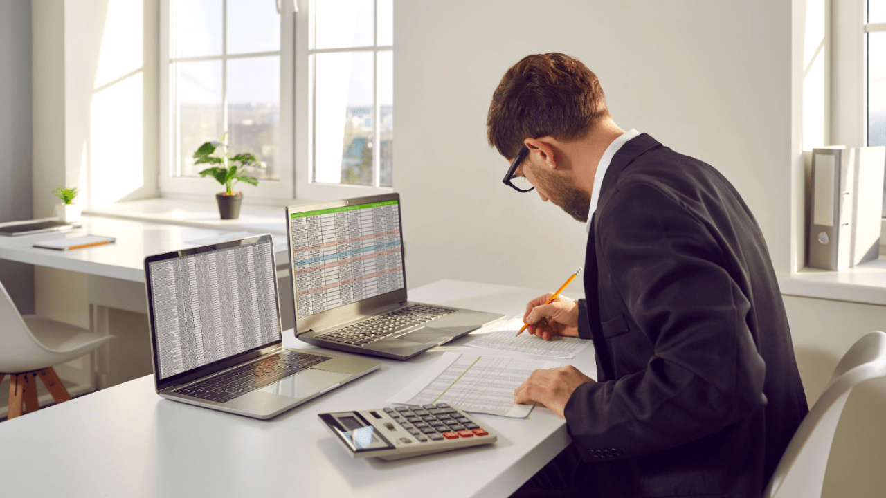 Financial analyst reviewing tax debt line items on spreadsheets while calculating obligations using dual monitor setup and calculator