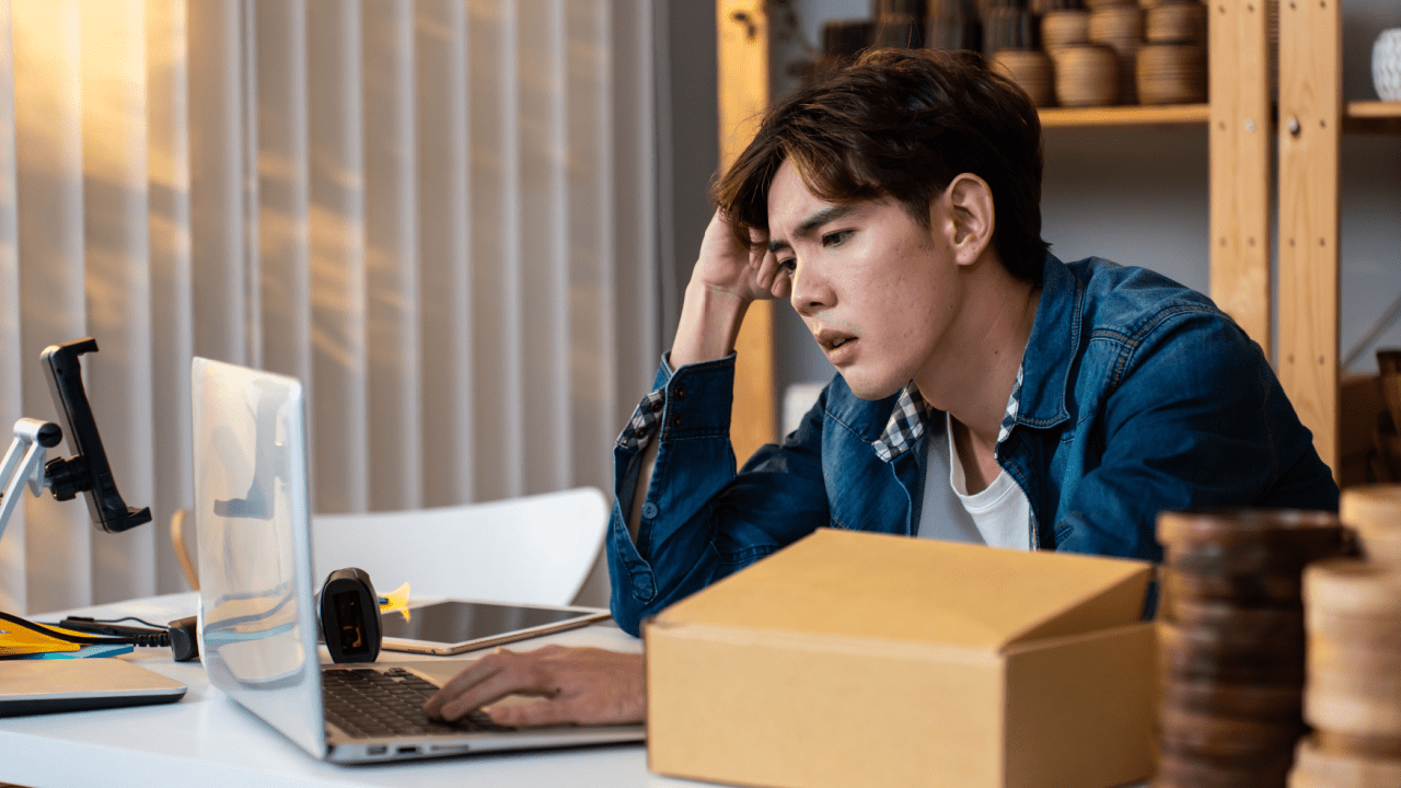 Overwhelmed small business owner researching tax debt uncollectible status while managing online business operations from home office
