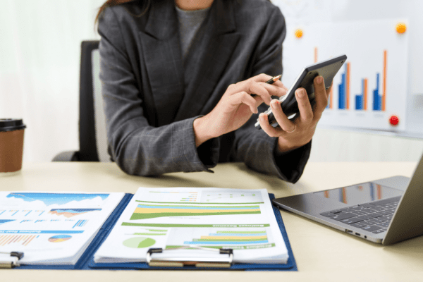 Business professional researching taxation of debt forgiveness using mobile device with financial charts and laptop
