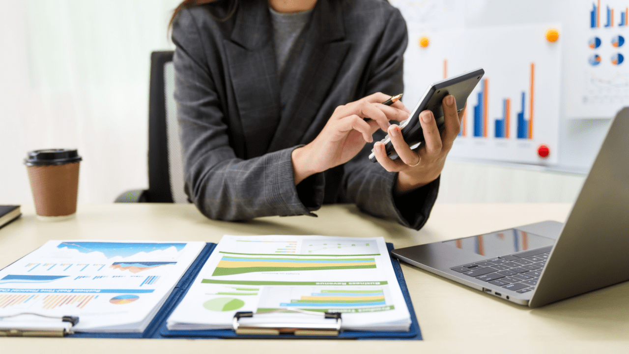 Business professional researching taxation of debt forgiveness using mobile device with financial charts and laptop