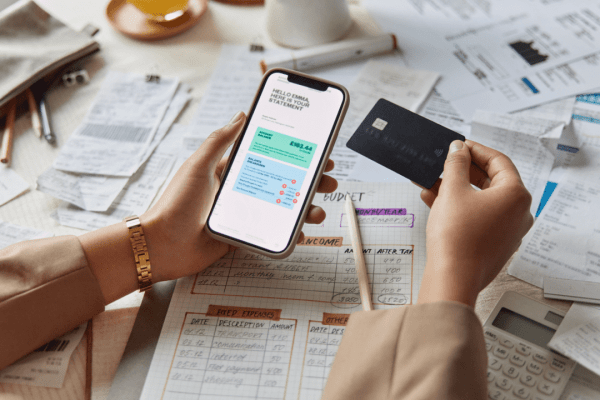 Person holding smartphone and credit card reviewing IRS payment plan options with tax documents and budget sheets on desk