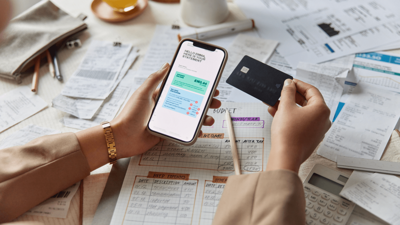 Person holding smartphone and credit card reviewing IRS payment plan options with tax documents and budget sheets on desk