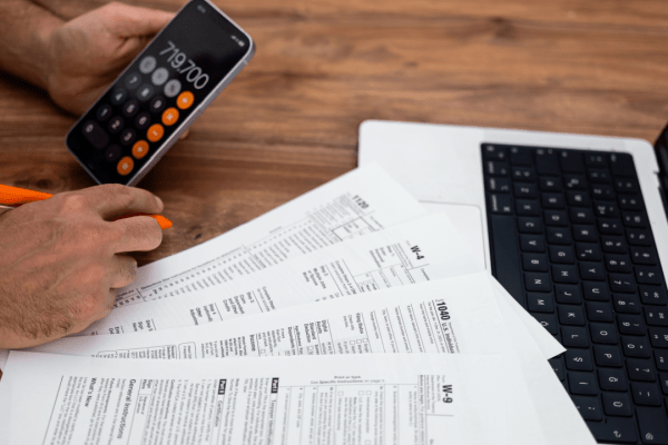 Person calculating tax debt with IRS forms, calculator app, and laptop while researching is the IRS forgiving tax debt in 2025 relief programs
