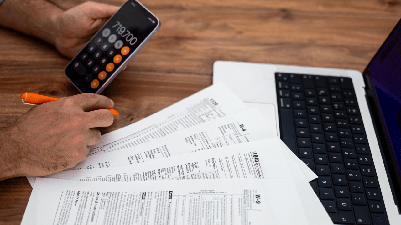 Person calculating tax debt with IRS forms, calculator app, and laptop while researching is the IRS forgiving tax debt in 2025 relief programs