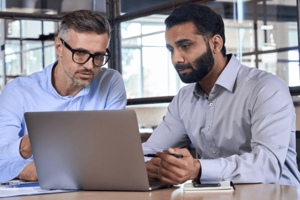 Two business professionals discussing when to hire a tax lawyer while reviewing financial documents on laptop