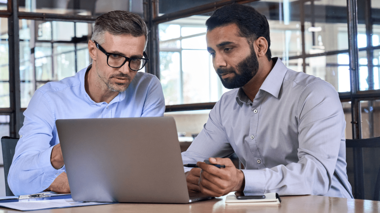 Two business professionals discussing when to hire a tax lawyer while reviewing financial documents on laptop