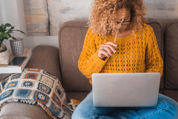 Woman researching tax attorney vs enrolled agent options on laptop while sitting on couch in thoughtful pose