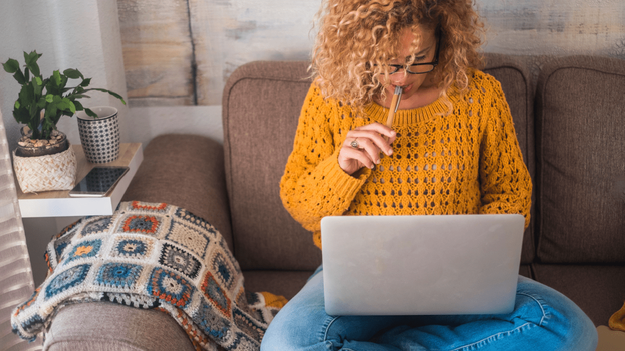 Woman researching tax attorney vs enrolled agent options on laptop while sitting on couch in thoughtful pose