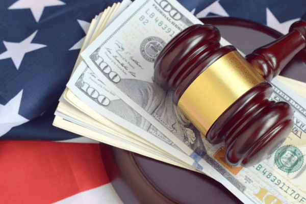 Wooden gavel and US dollar bills on American flag representing factors that affect tax attorney fees