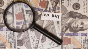 Magnifying glass and "Tax Day" note on prop US currency bills illustrating how much money do you have to owe the IRS before you go to jail