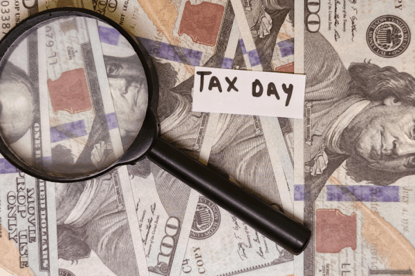 Magnifying glass and "Tax Day" note on prop US currency bills illustrating how much money do you have to owe the IRS before you go to jail