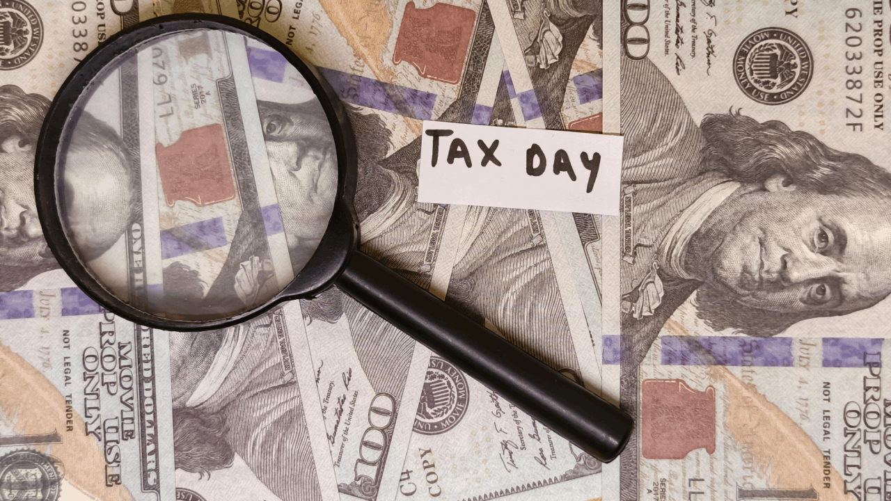 Magnifying glass and "Tax Day" note on prop US currency bills illustrating how much money do you have to owe the IRS before you go to jail