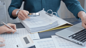 A tax professional reviewing financial documents with a magnifying glass during an IRS audit, illustrating what happens if you get audited and your taxes are wrong