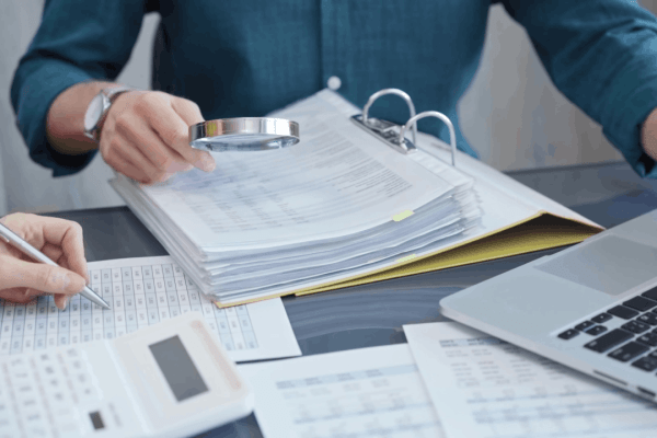A tax professional reviewing financial documents with a magnifying glass during an IRS audit, illustrating what happens if you get audited and your taxes are wrong