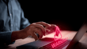 A person typing on a laptop with a glowing red warning symbol — representing what income level triggers an audit and the urgency of IRS audit risk