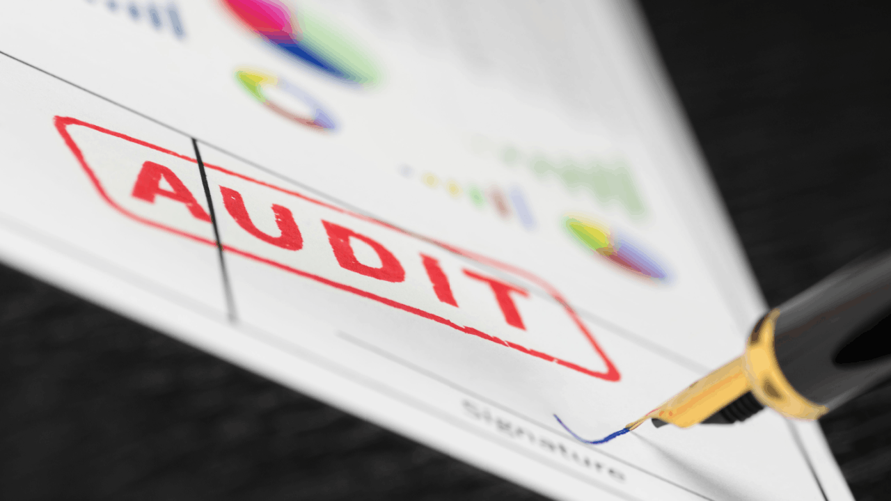 A document stamped with the word AUDIT in red ink beside a pen, representing what is most likely to trigger an IRS audit in 2026