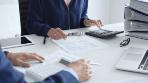 Two professionals reviewing tax documents with a magnifying glass and calculator during a tax audit meeting