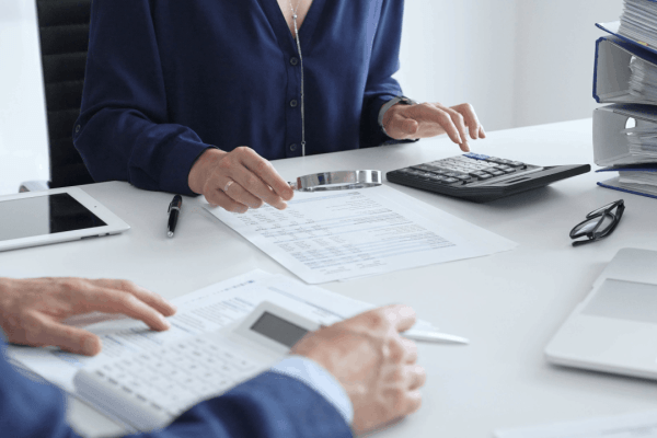 Two professionals reviewing tax documents with a magnifying glass and calculator during a tax audit meeting